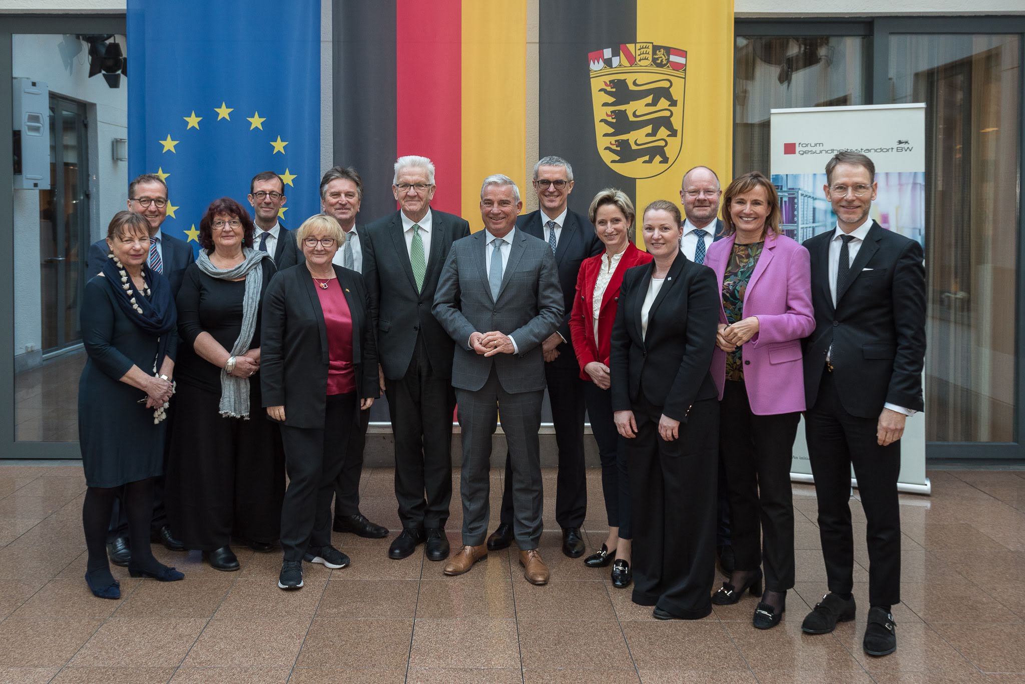 Eine Gruppe baden-württembergischer Politiker versammelt sich für ein Gruppenfoto vor den Fahnen von Deutschland und Europa.